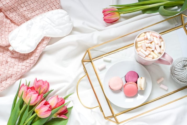 Breakfast in bed pastel flat lay composition with flowers, a cup o coffee and sweets. Concept woman's or mother's day top view